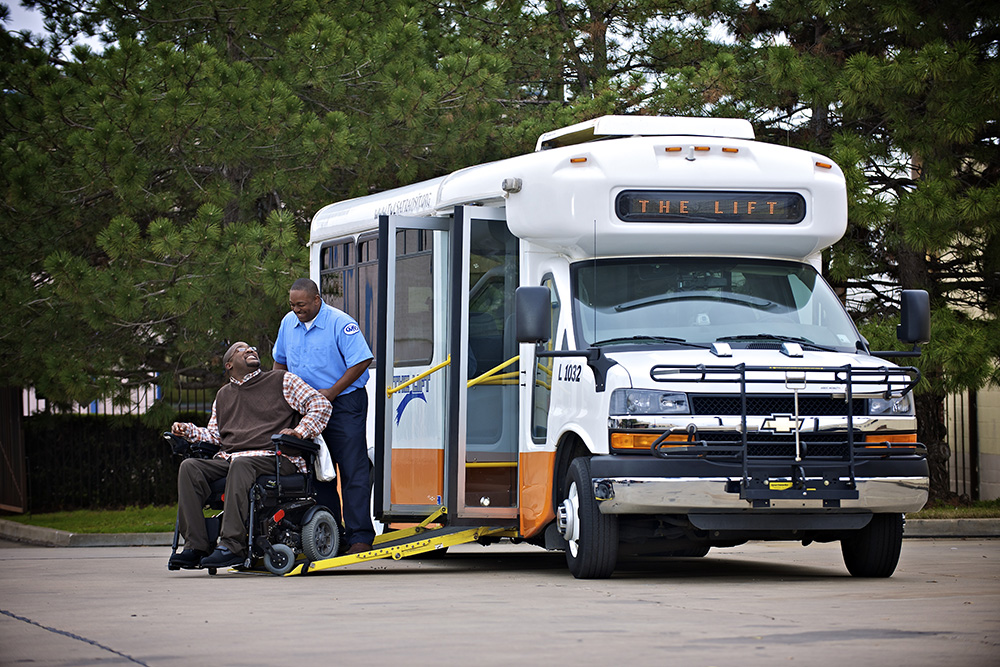 Bus operator helping a man in mobility chair into bus
